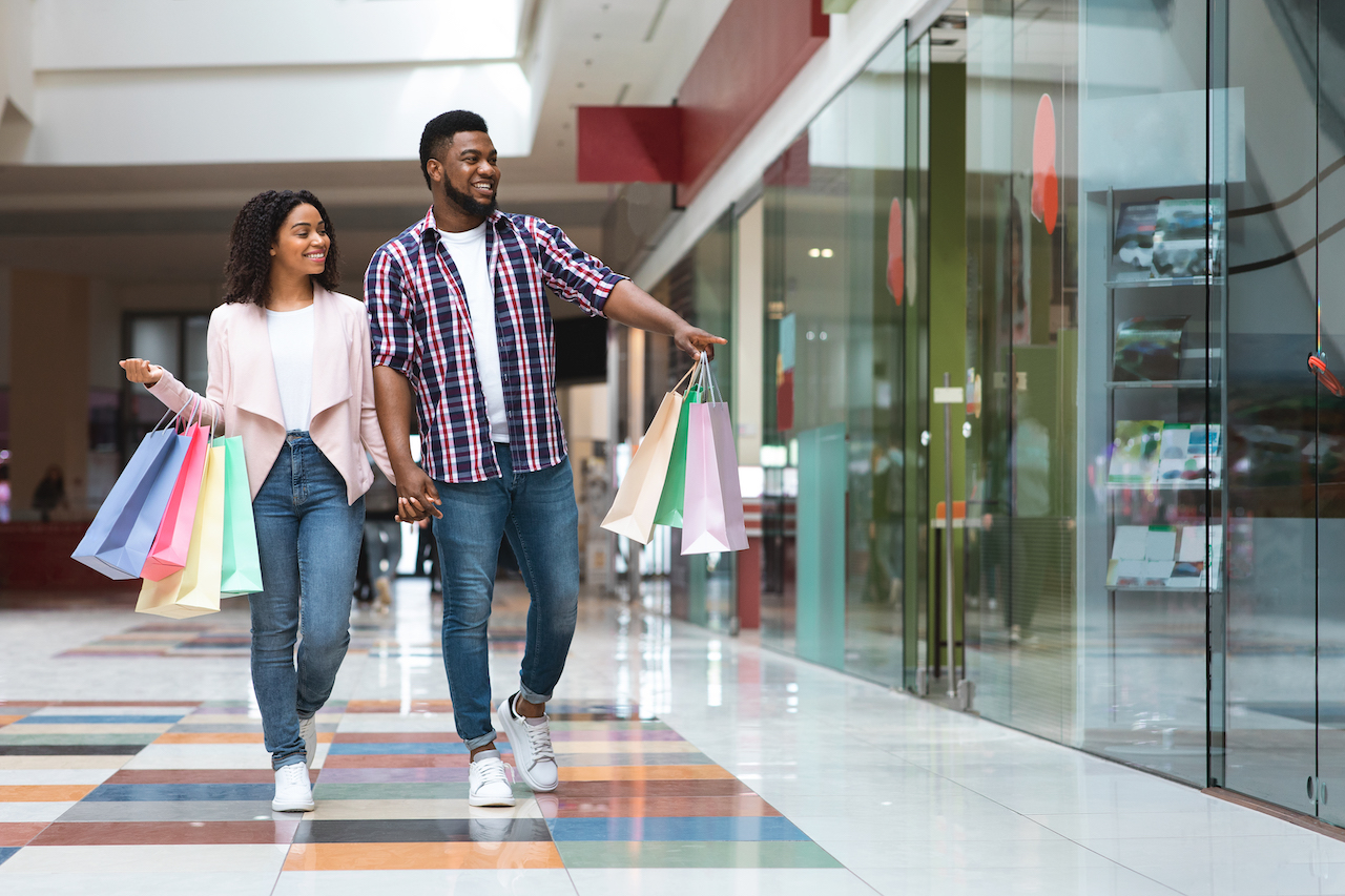 Happy black man showing something in shop window to his girlfriend